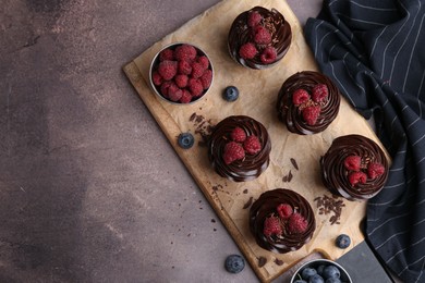 Photo of Tasty cupcakes with chocolate cream and berries on brown table, flat lay. Space for text