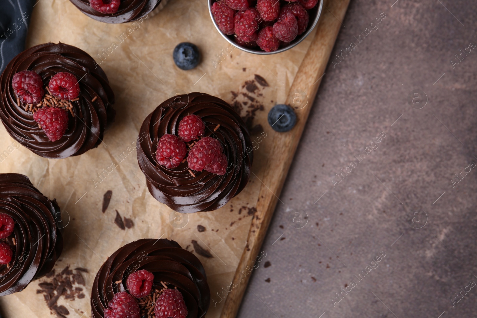 Photo of Tasty cupcakes with chocolate cream and berries on brown table, flat lay. Space for text