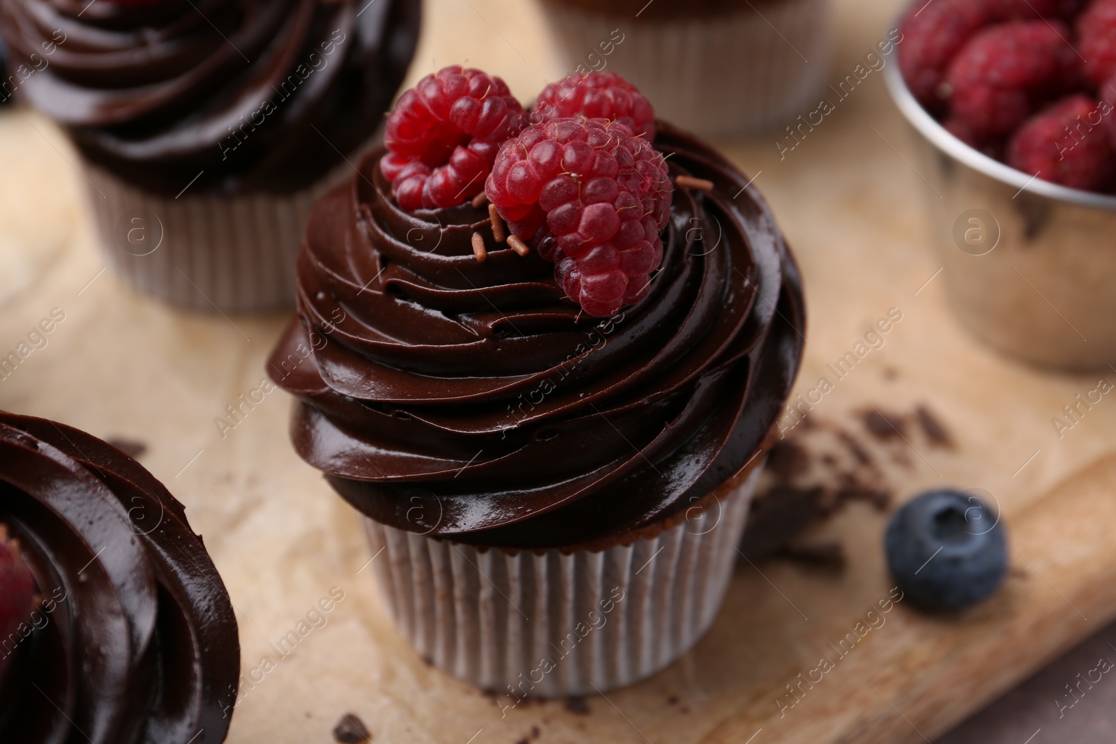 Photo of Tasty cupcakes with chocolate cream and berries on brown table, closeup