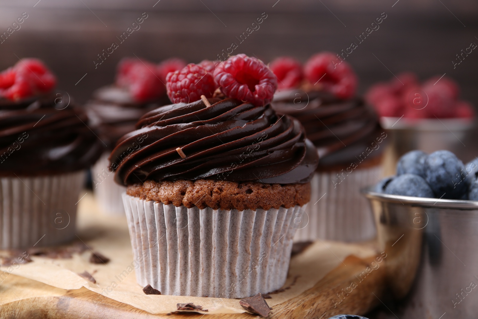 Photo of Tasty cupcakes with chocolate cream and berries on wooden board, closeup