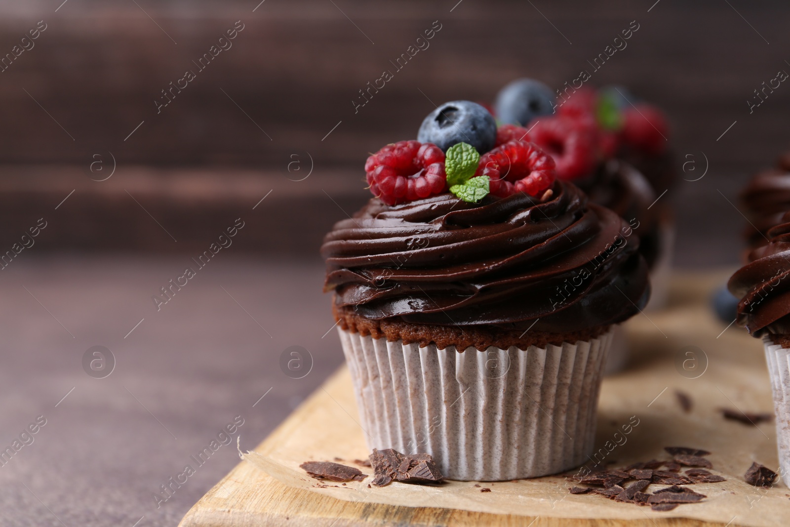 Photo of Tasty cupcakes with chocolate cream and berries on brown table, closeup. Space for text