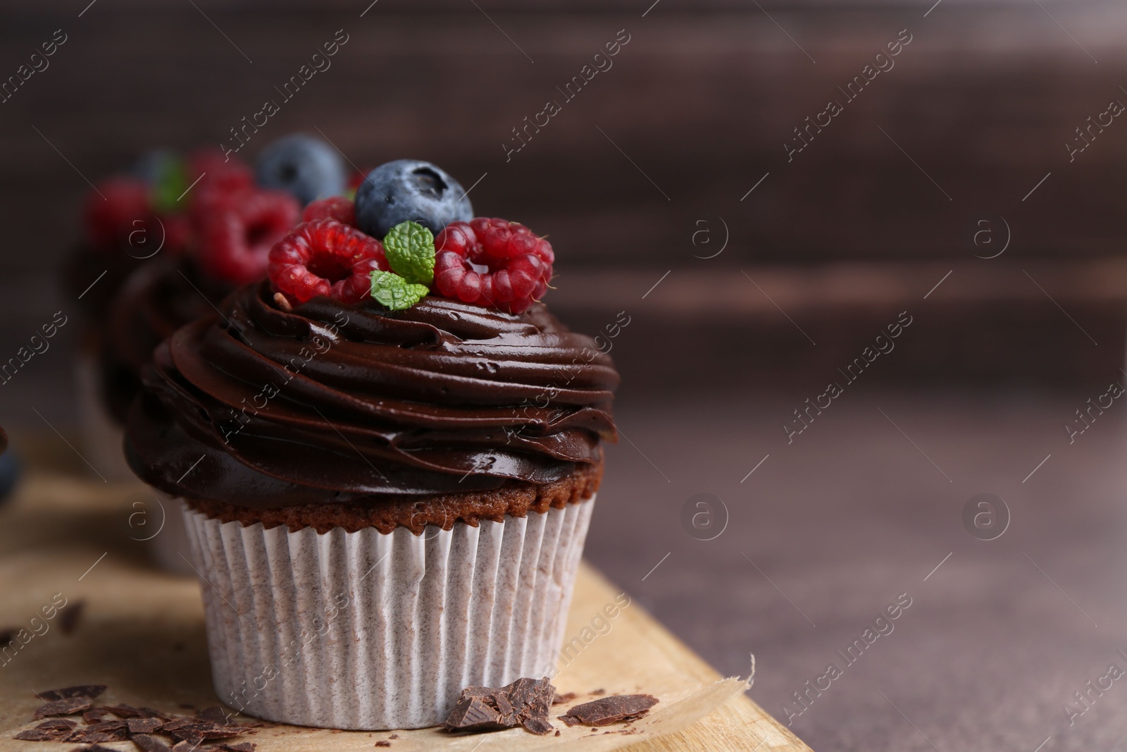 Photo of Tasty cupcakes with chocolate cream and berries on brown table, closeup. Space for text