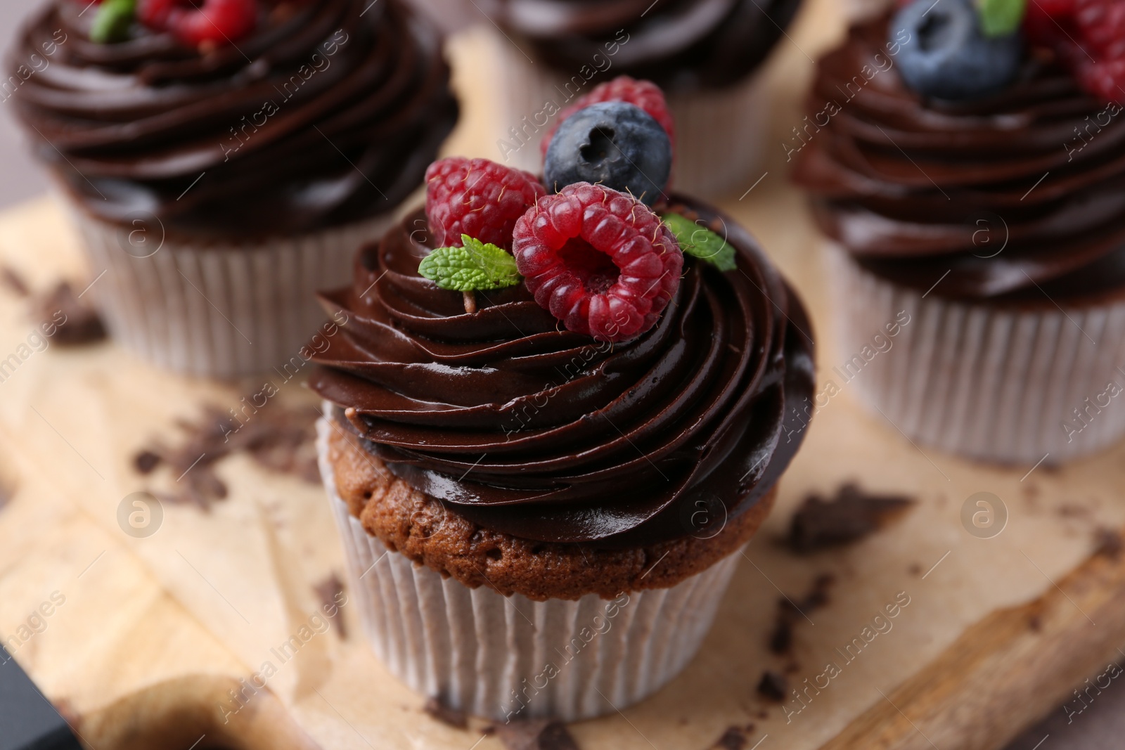 Photo of Tasty cupcakes with chocolate cream and berries on wooden board, closeup