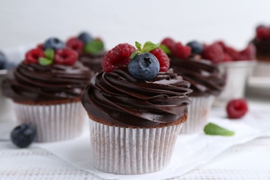 Photo of Tasty cupcakes with chocolate cream and berries on white wooden table, closeup