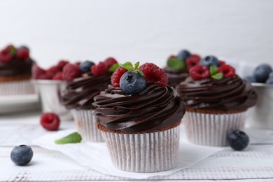 Photo of Tasty cupcakes with chocolate cream and berries on white wooden table, closeup