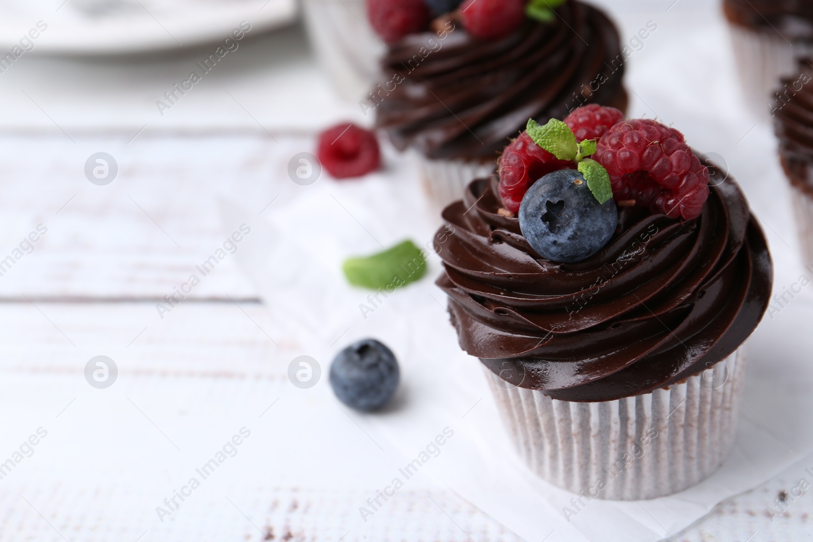 Photo of Tasty cupcakes with chocolate cream and berries on white wooden table, closeup. Space for text