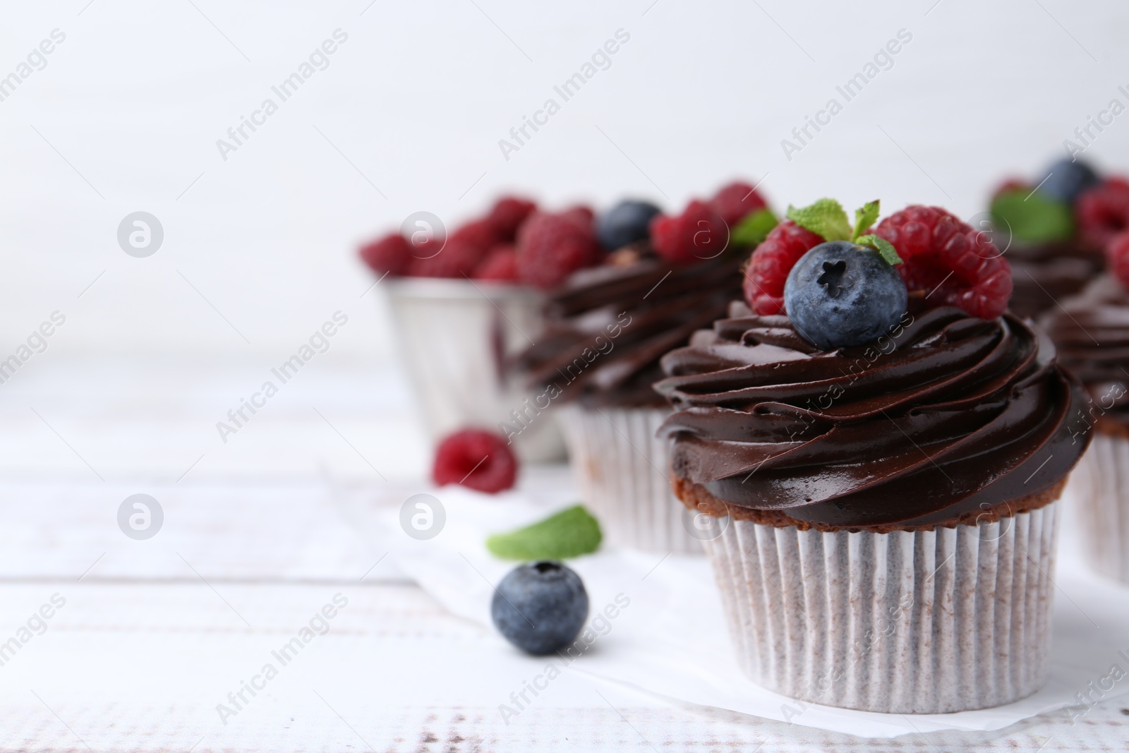 Photo of Tasty cupcakes with chocolate cream and berries on white wooden table, closeup. Space for text