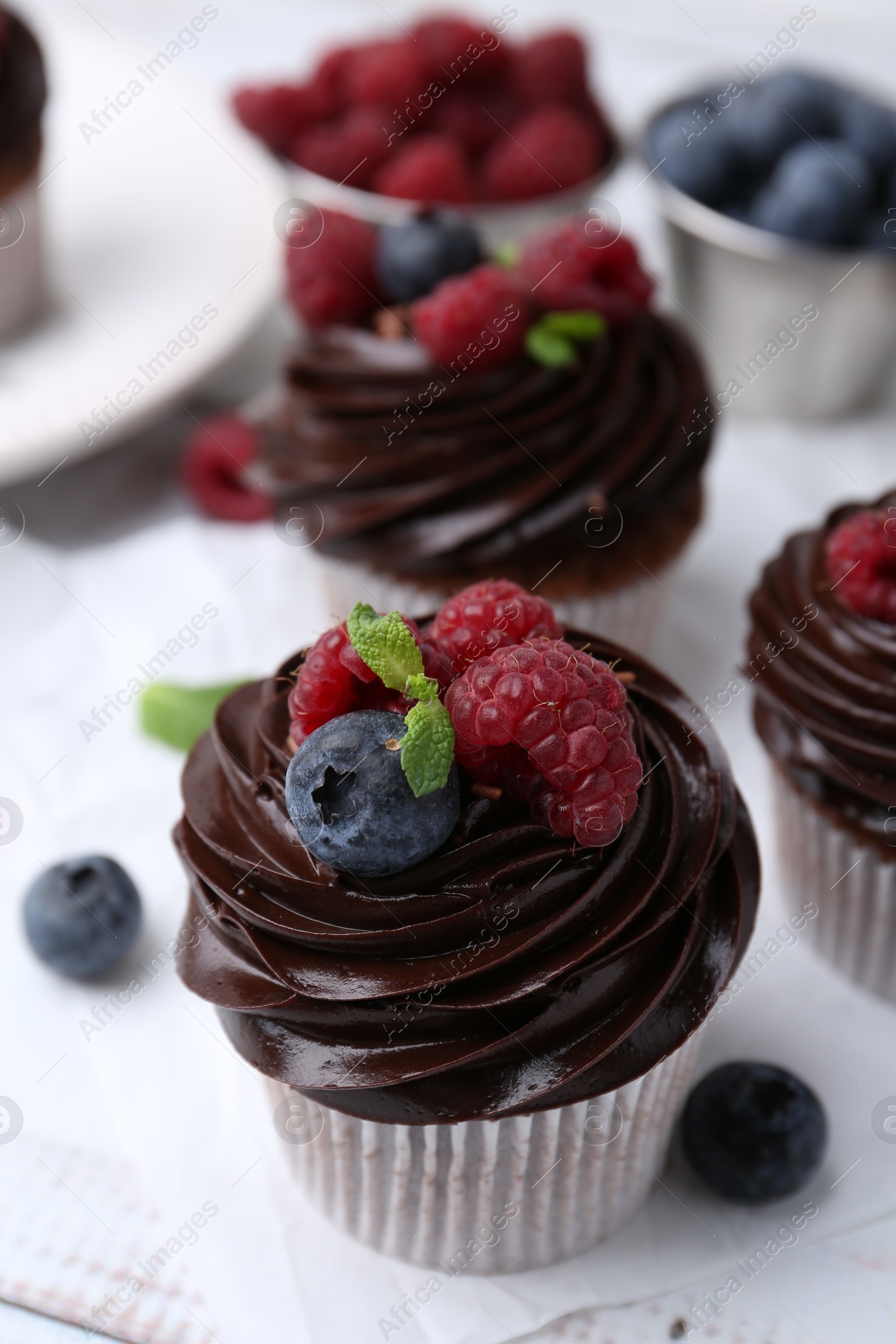 Photo of Tasty cupcakes with chocolate cream and berries on white wooden table, closeup