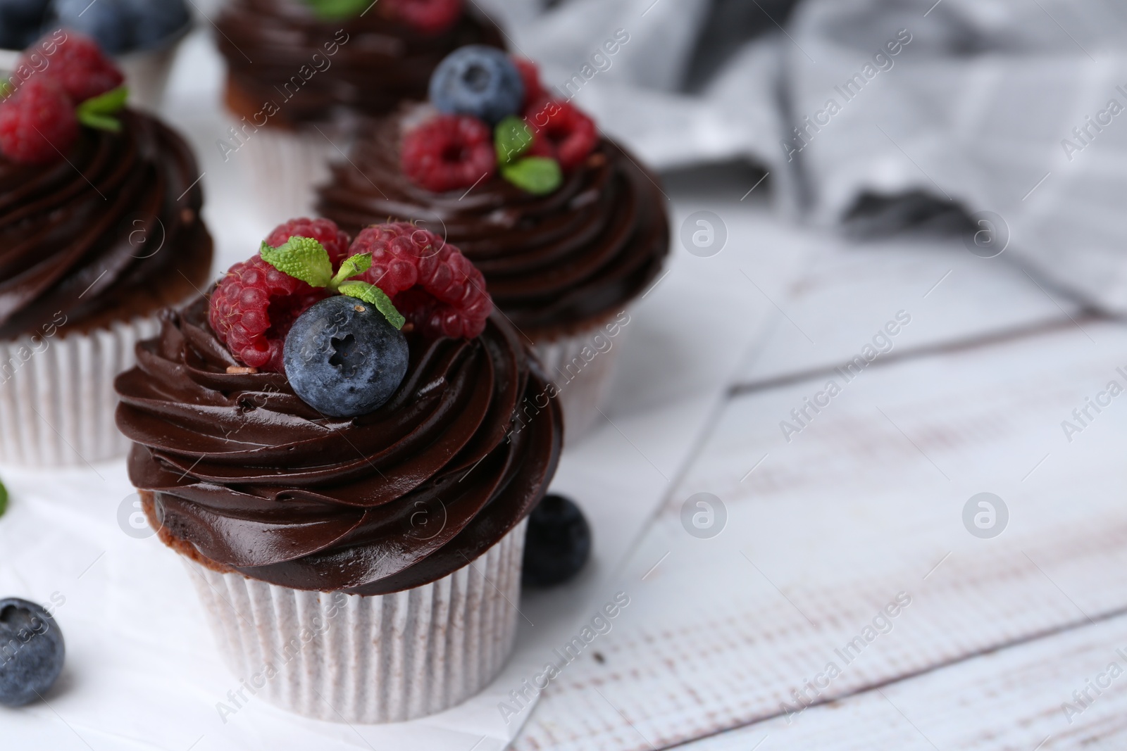 Photo of Tasty cupcakes with chocolate cream and berries on white wooden table, closeup. Space for text