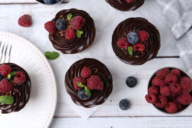 Photo of Tasty cupcakes with chocolate cream and berries on white wooden table, flat lay