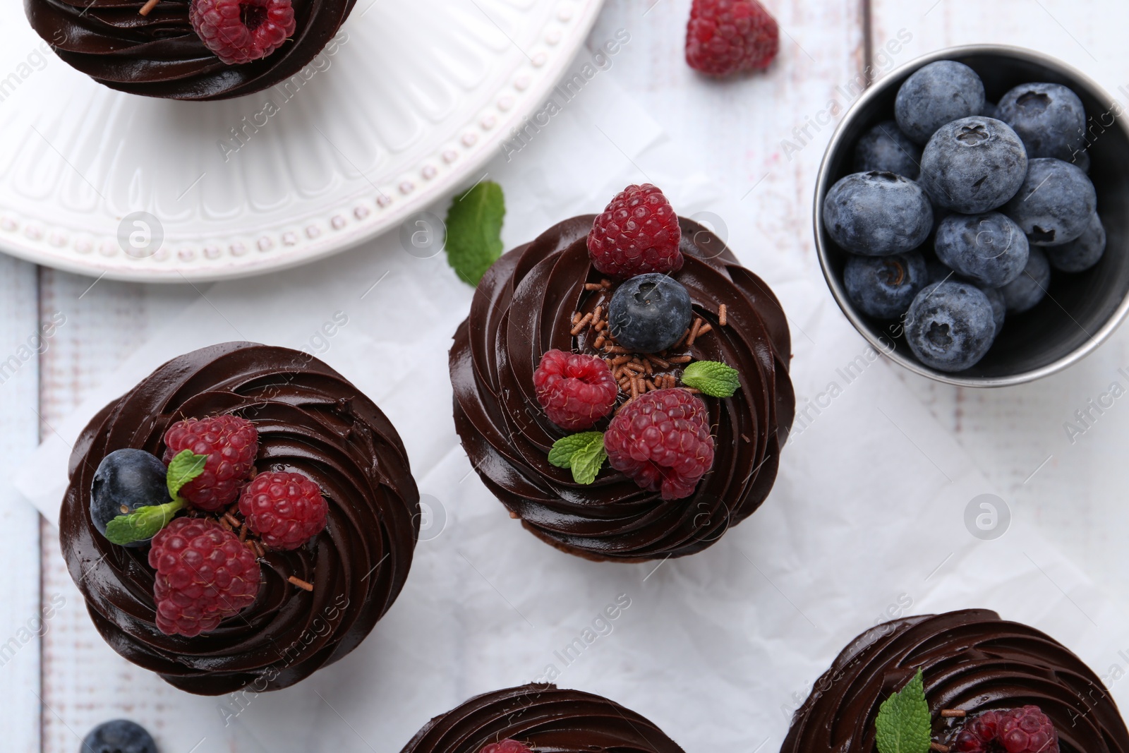 Photo of Tasty cupcakes with chocolate cream and berries on white wooden table, flat lay