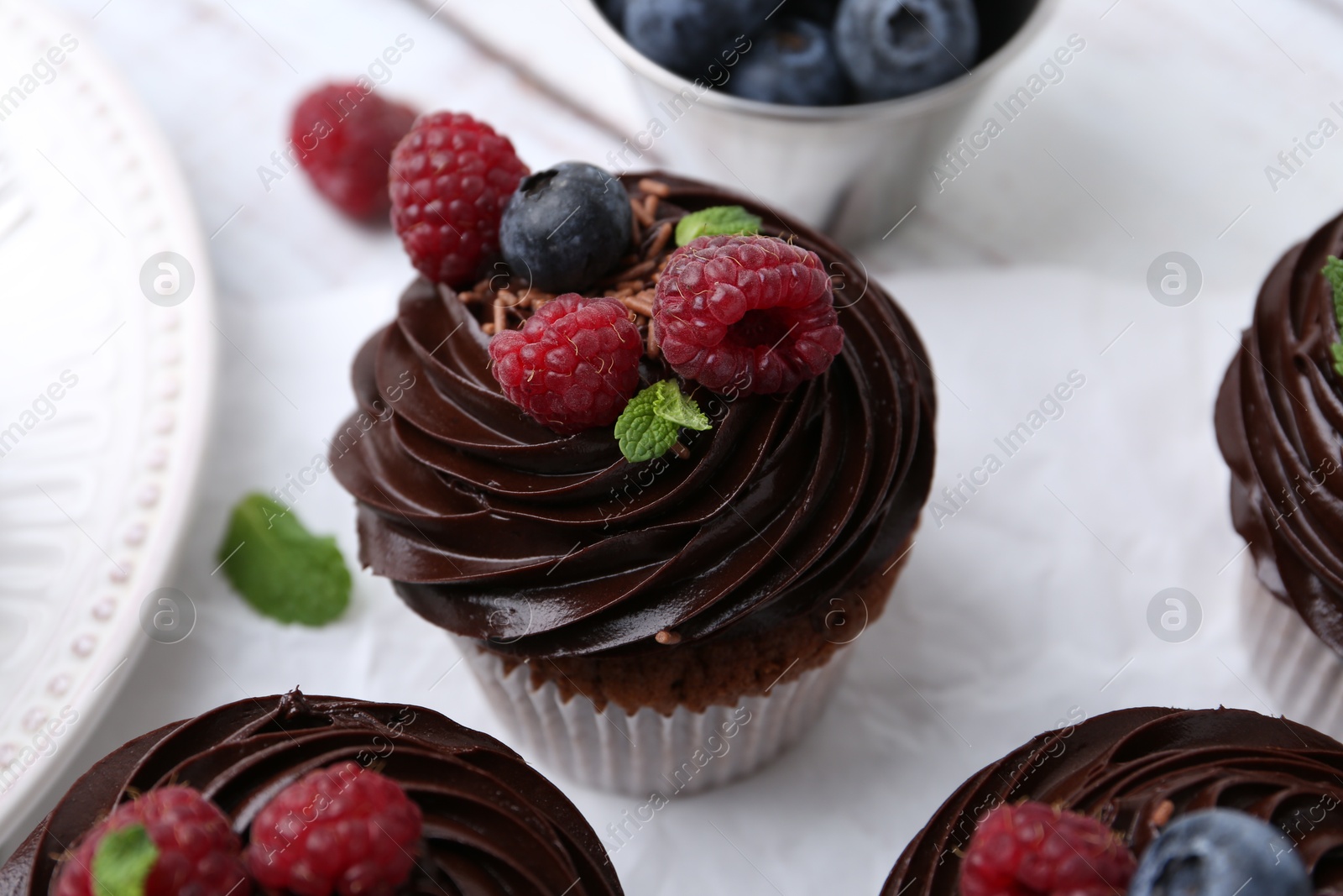 Photo of Tasty cupcakes with chocolate cream and berries on white wooden table, closeup