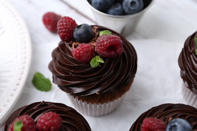 Photo of Tasty cupcakes with chocolate cream and berries on white wooden table, closeup