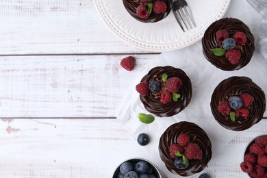 Photo of Tasty cupcakes with chocolate cream and berries on white wooden table, flat lay. Space for text