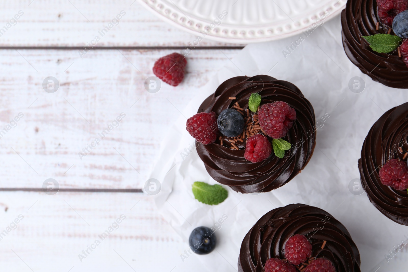 Photo of Tasty cupcakes with chocolate cream and berries on white wooden table, flat lay. Space for text