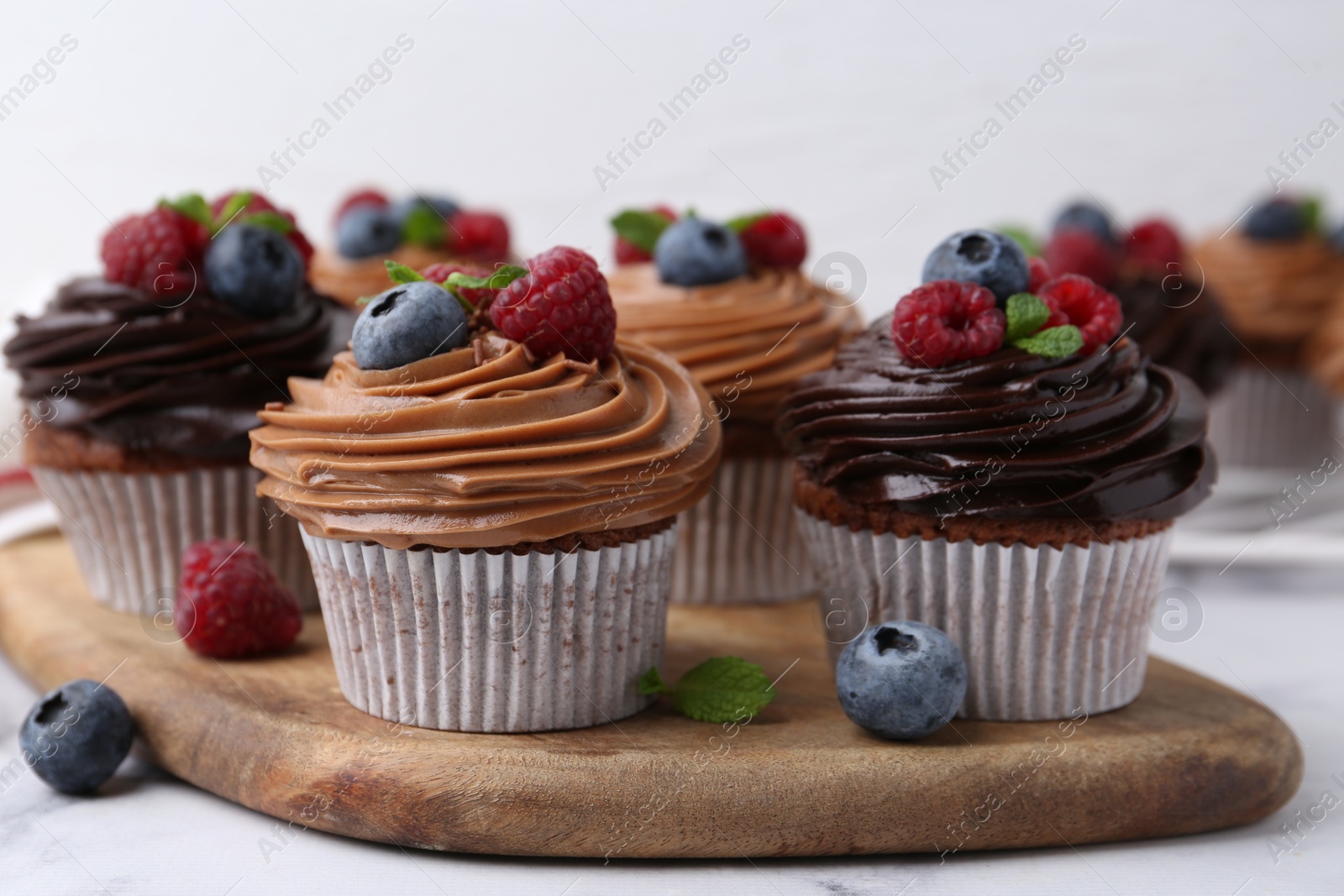 Photo of Tasty cupcakes with chocolate cream and berries on white marble table, closeup