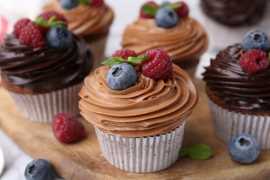 Photo of Tasty cupcakes with chocolate cream and berries on white table, closeup