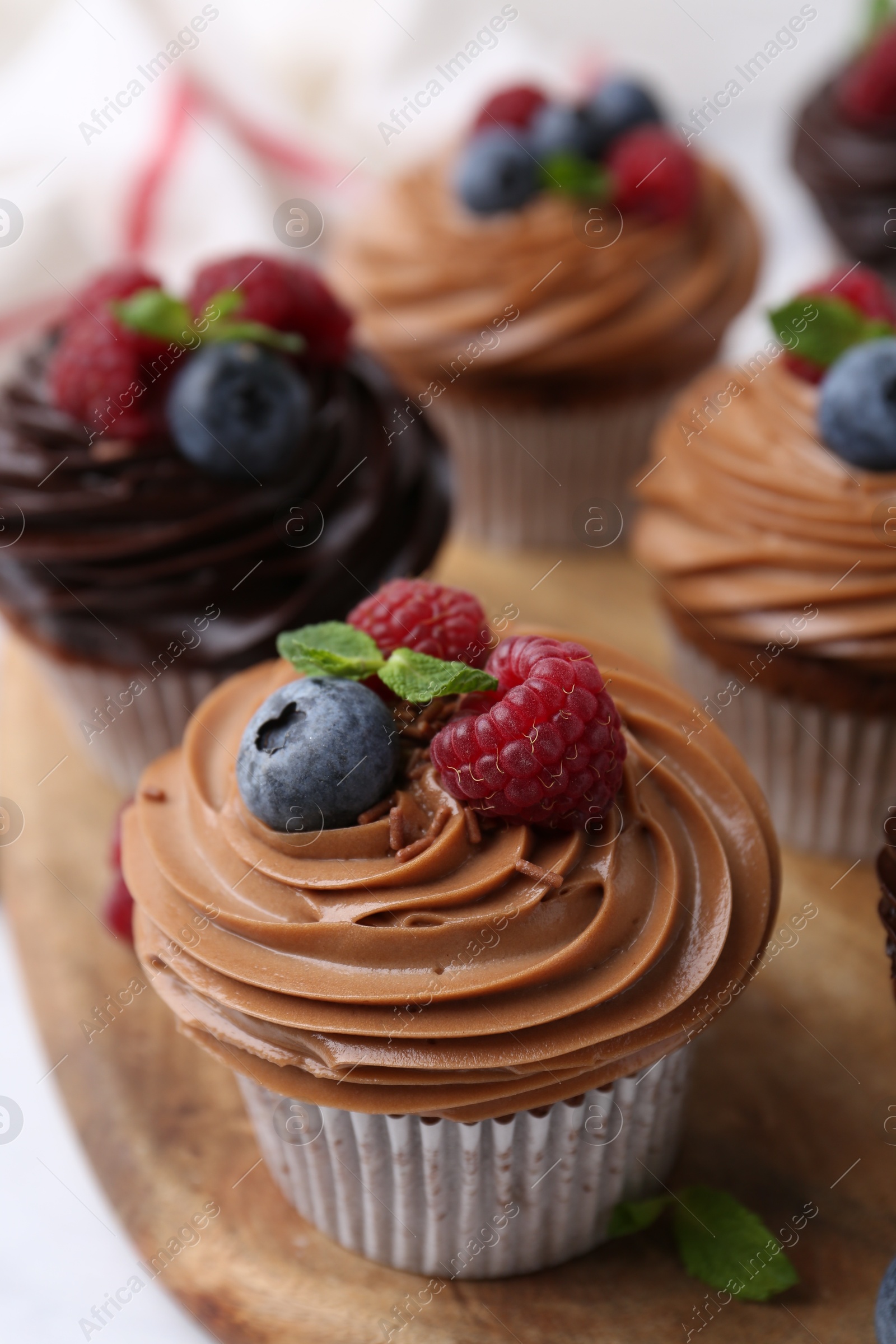 Photo of Tasty cupcakes with chocolate cream and berries on white table, closeup