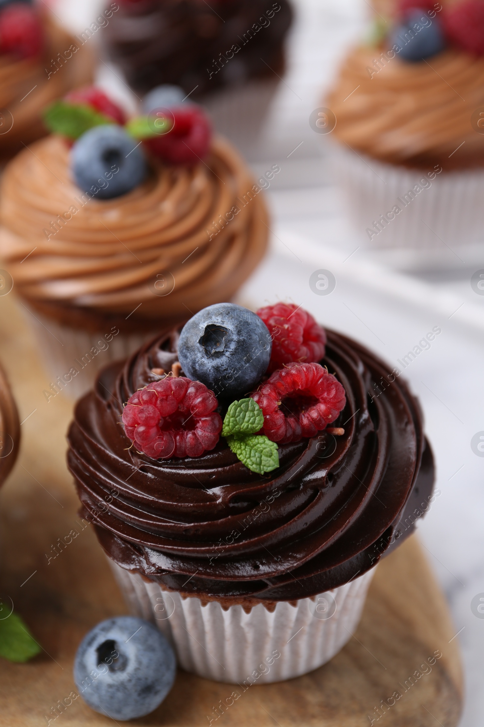 Photo of Tasty cupcakes with chocolate cream and berries on white marble table, closeup