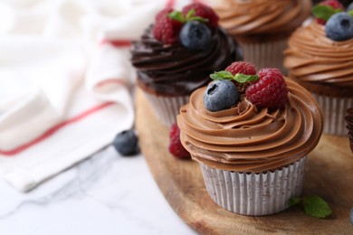 Photo of Tasty cupcakes with chocolate cream and berries on white marble table, closeup. Space for text