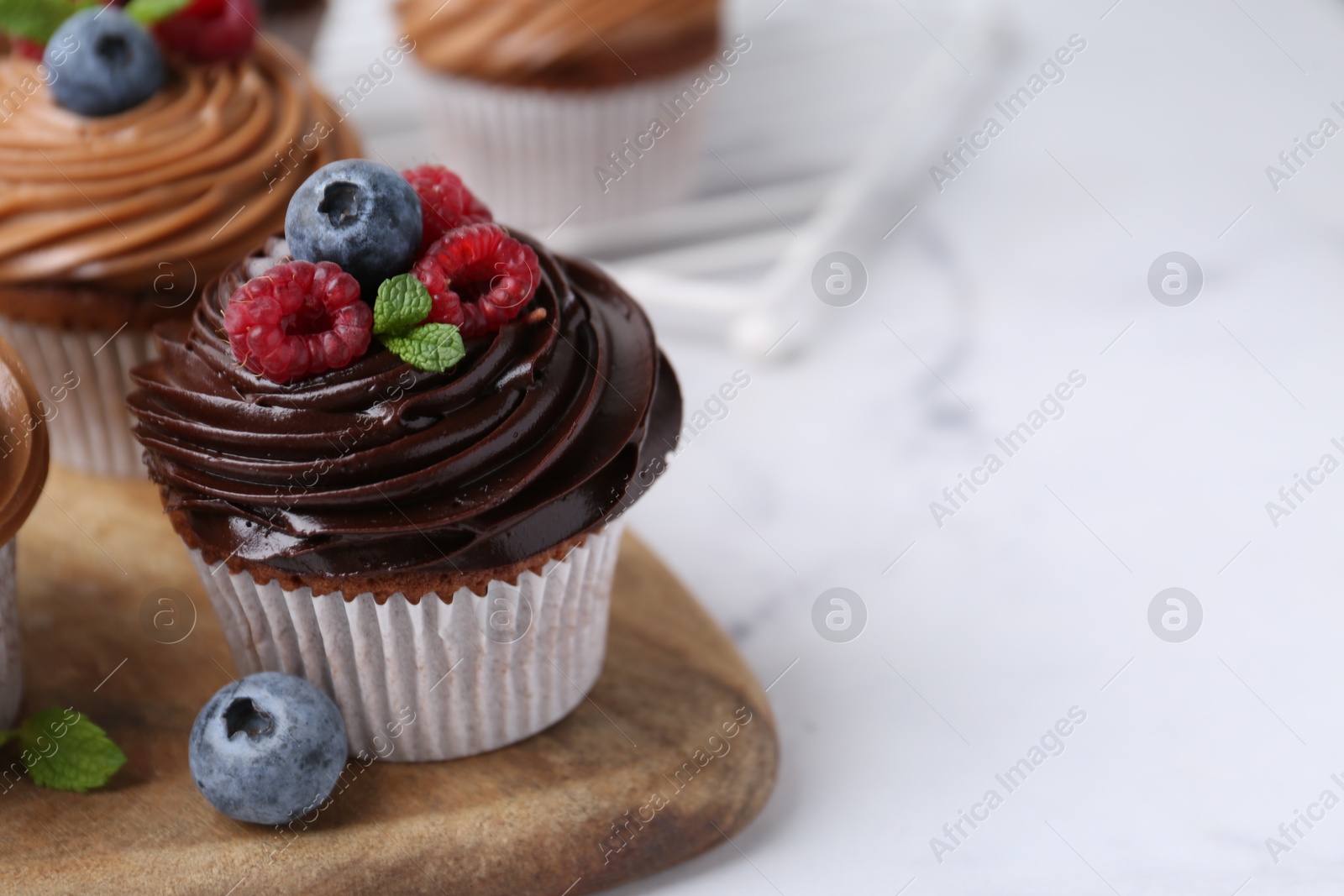 Photo of Tasty cupcakes with chocolate cream and berries on white marble table, closeup. Space for text