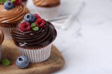 Photo of Tasty cupcakes with chocolate cream and berries on white marble table, closeup. Space for text