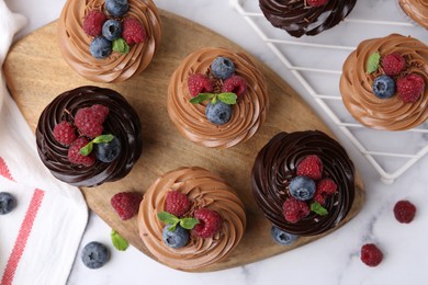 Photo of Tasty cupcakes with chocolate cream and berries on white marble table, flat lay