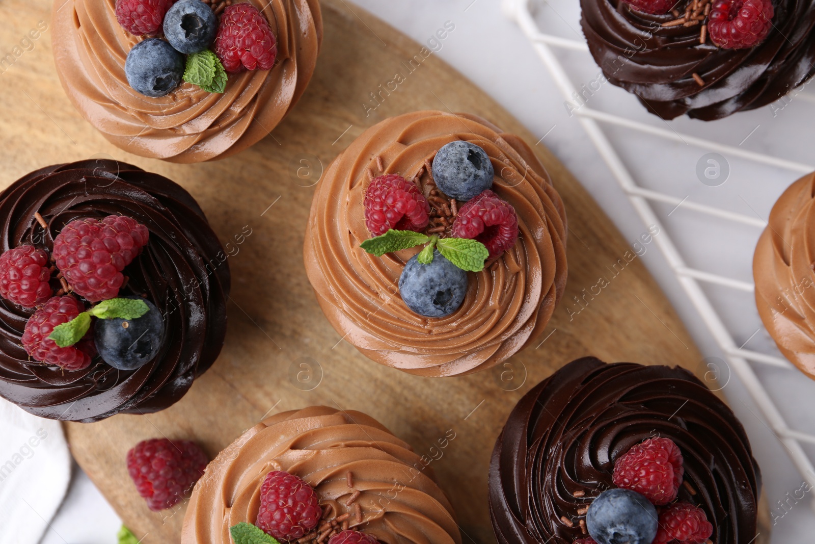 Photo of Tasty cupcakes with chocolate cream and berries on white marble table, flat lay