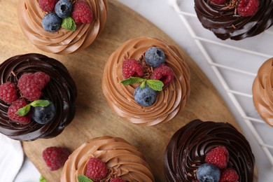 Photo of Tasty cupcakes with chocolate cream and berries on white marble table, flat lay