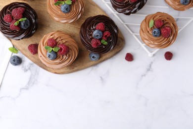 Photo of Tasty cupcakes with chocolate cream and berries on white marble table, flat lay. Space for text