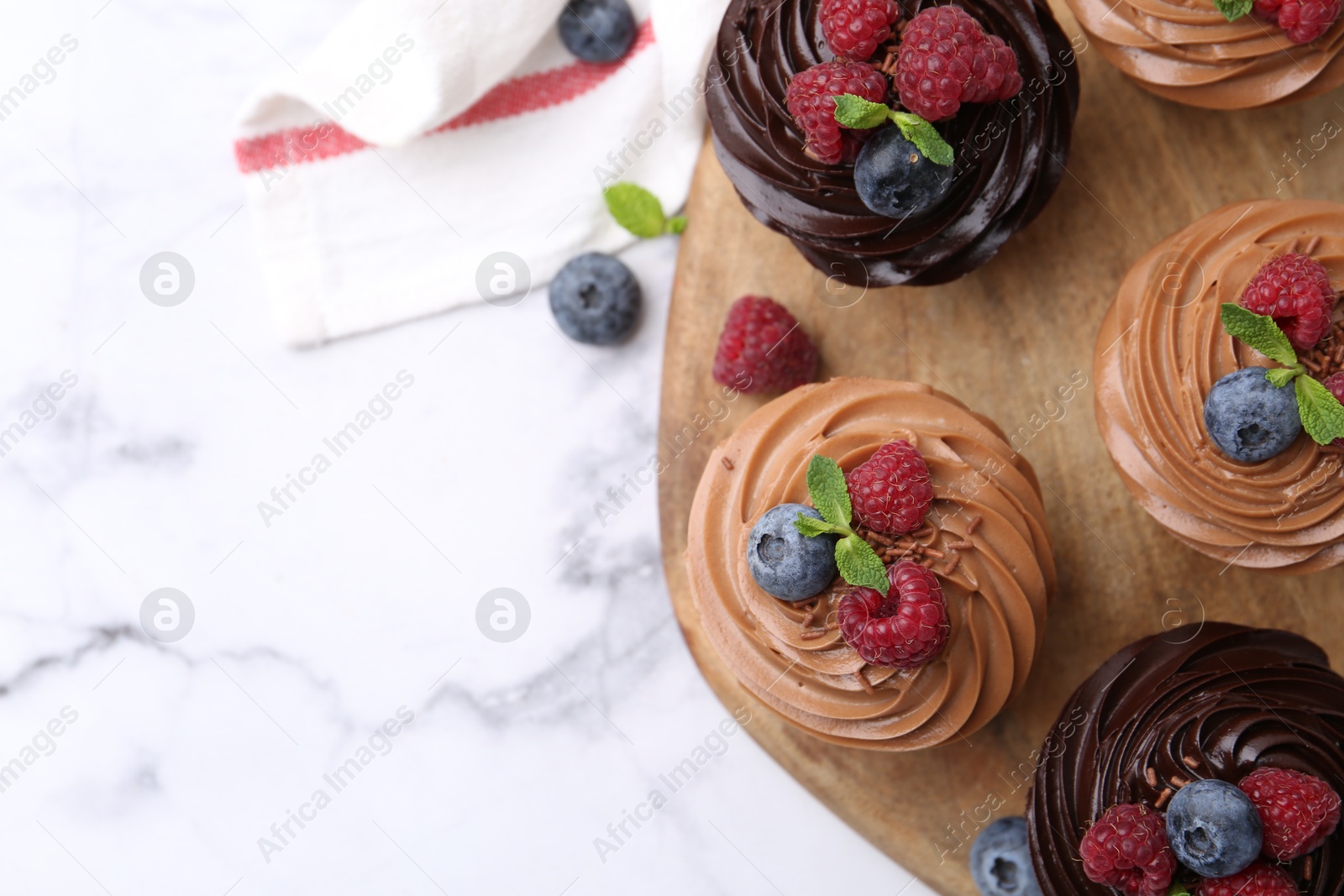 Photo of Tasty cupcakes with chocolate cream and berries on white marble table, flat lay. Space for text