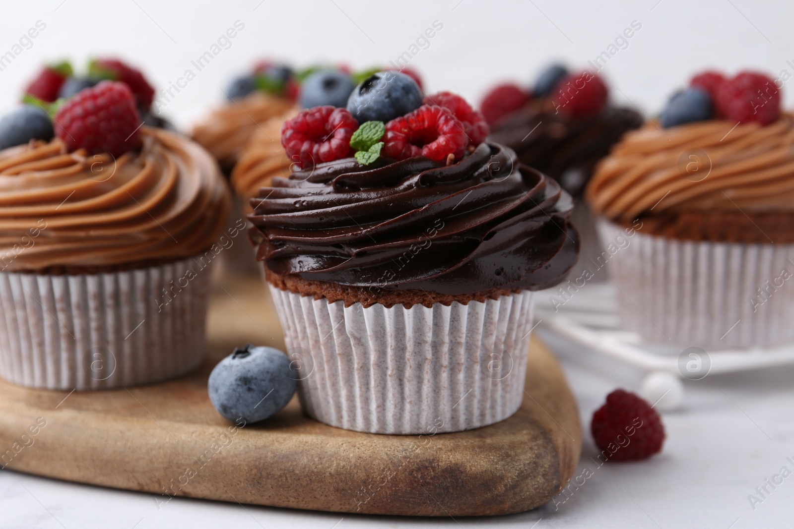 Photo of Tasty cupcakes with chocolate cream and berries on white marble table, closeup