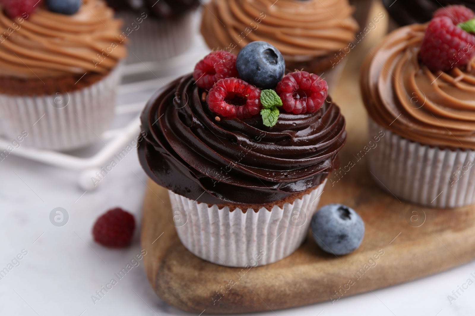 Photo of Tasty cupcakes with chocolate cream and berries on white marble table, closeup