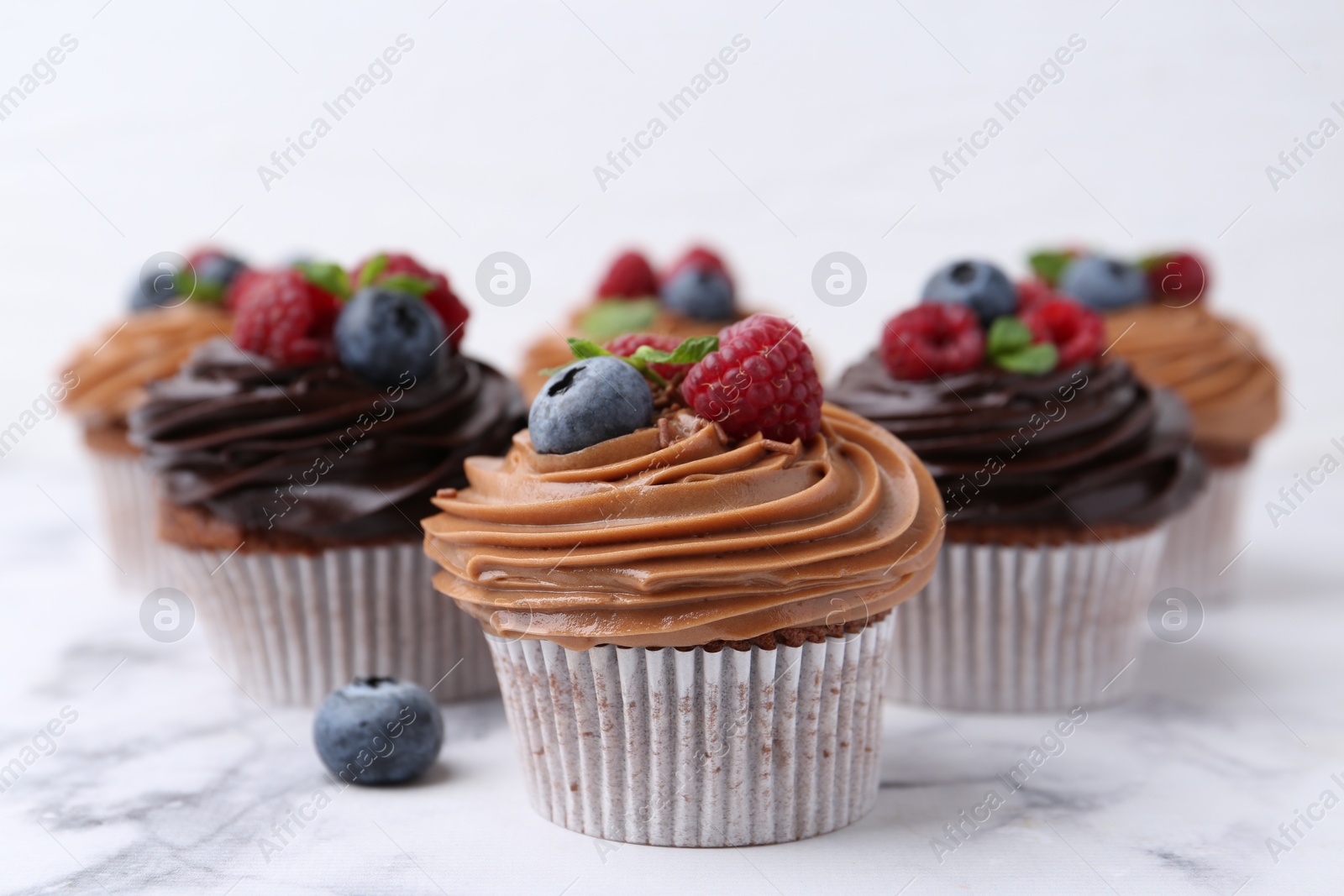 Photo of Tasty cupcakes with chocolate cream and berries on white marble table, closeup