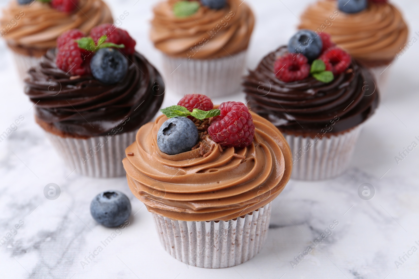 Photo of Tasty cupcakes with chocolate cream and berries on white marble table, closeup