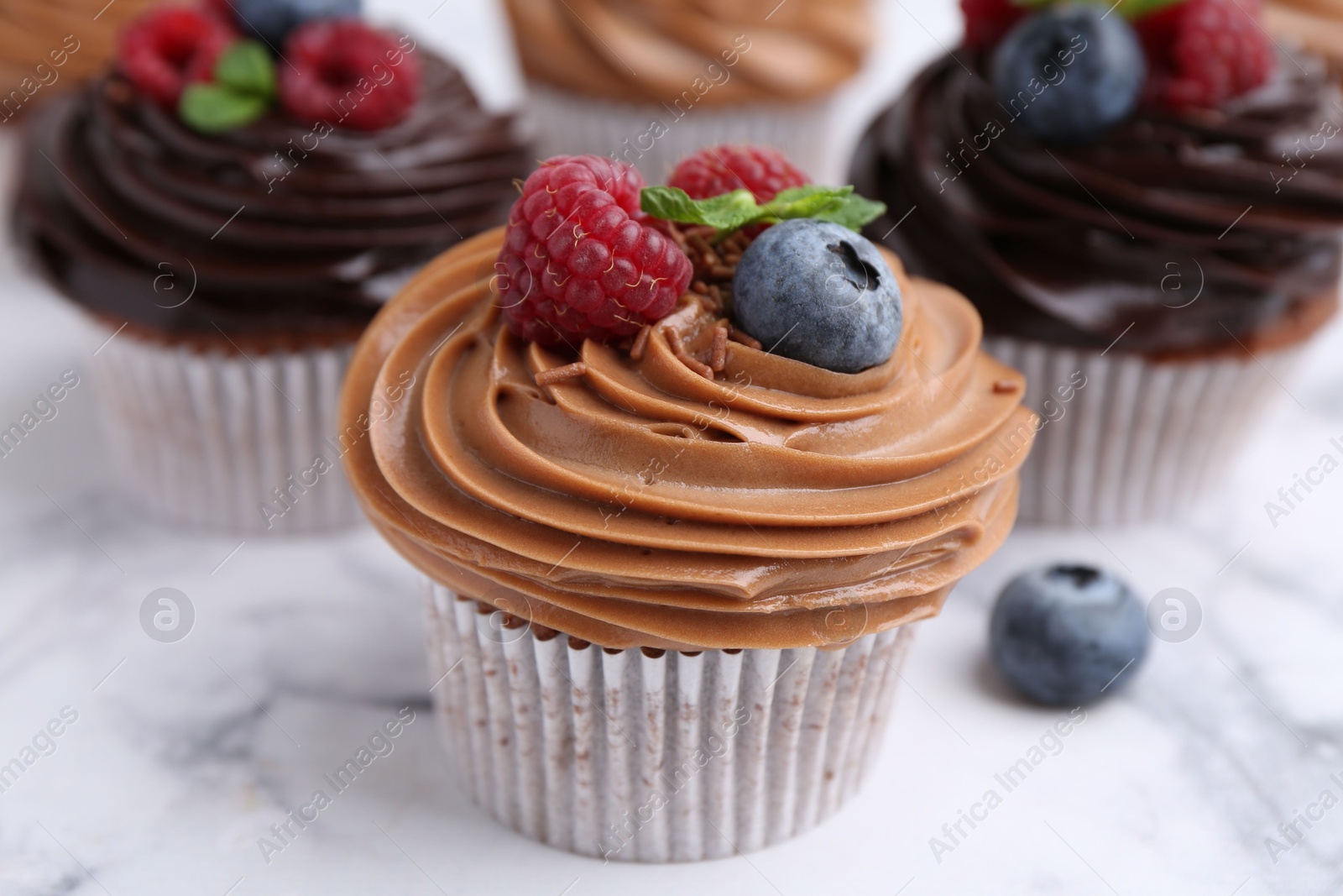 Photo of Tasty cupcakes with chocolate cream and berries on white marble table, closeup