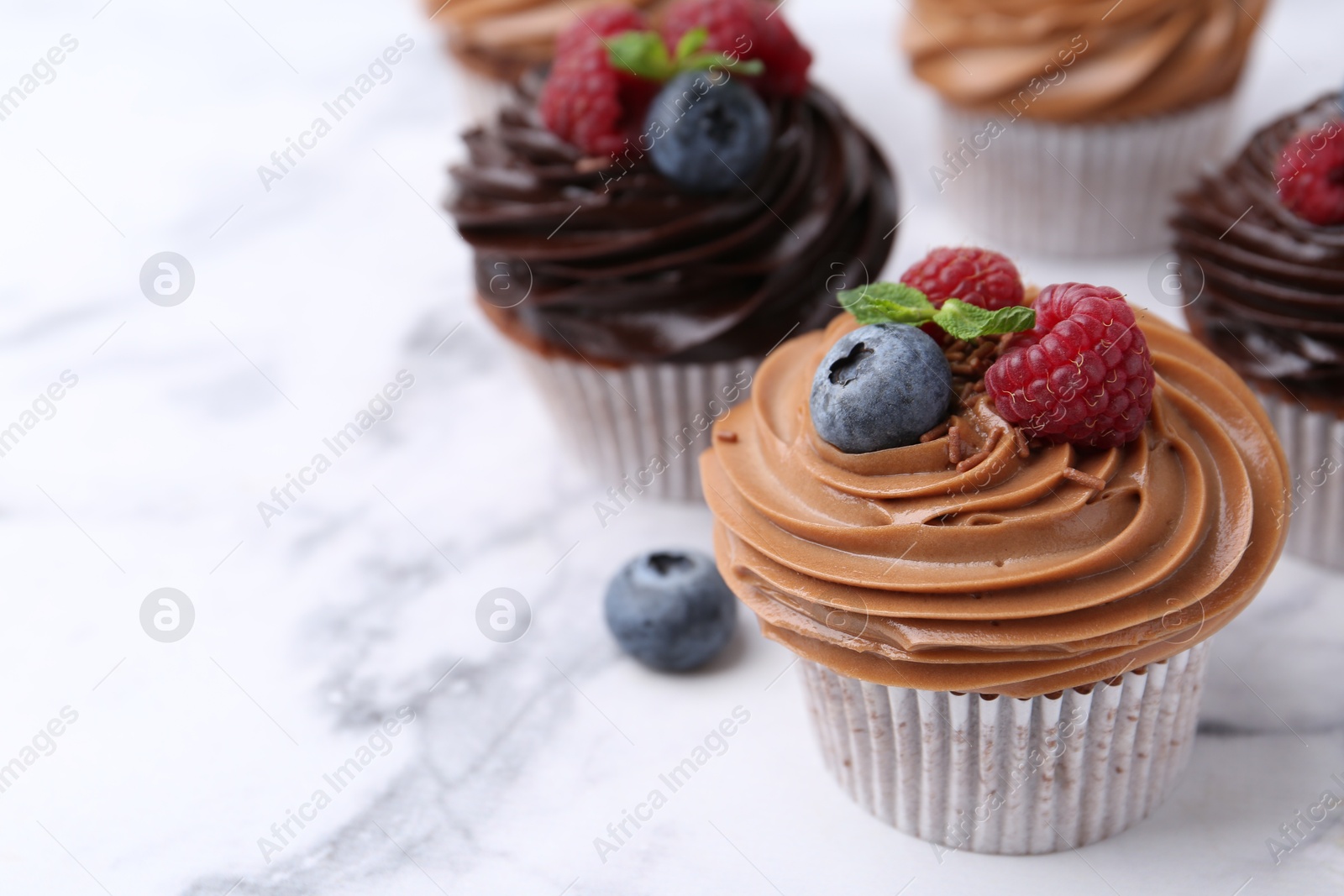 Photo of Tasty cupcakes with chocolate cream and berries on white marble table, closeup. Space for text