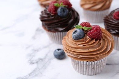 Photo of Tasty cupcakes with chocolate cream and berries on white marble table, closeup. Space for text