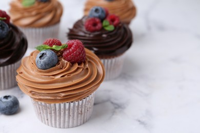 Photo of Tasty cupcakes with chocolate cream and berries on white marble table, closeup. Space for text