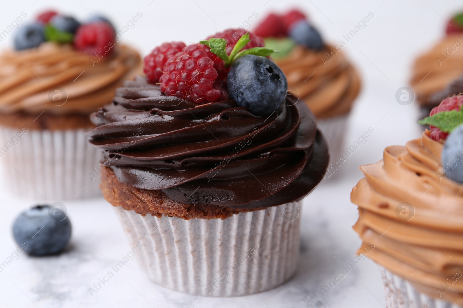 Photo of Tasty cupcakes with chocolate cream and berries on white marble table, closeup