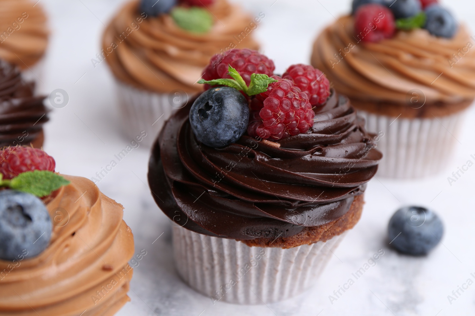 Photo of Tasty cupcakes with chocolate cream and berries on white marble table, closeup