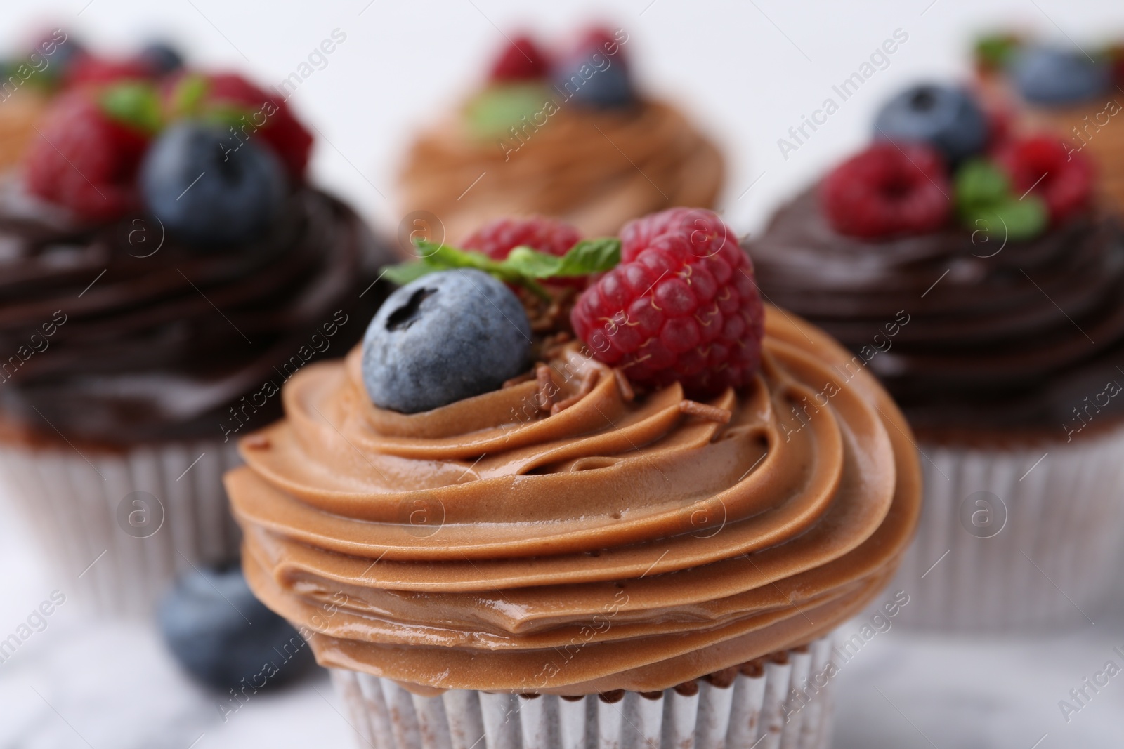 Photo of Tasty cupcakes with chocolate cream and berries on white table, closeup