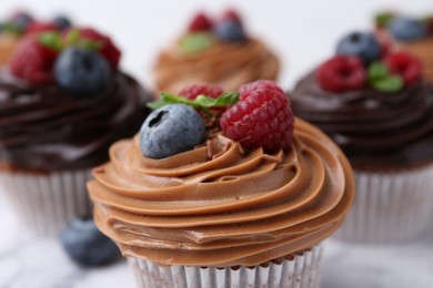 Photo of Tasty cupcakes with chocolate cream and berries on white table, closeup