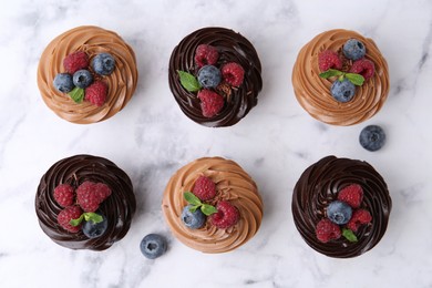 Photo of Tasty cupcakes with chocolate cream and berries on white marble table, flat lay