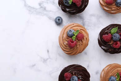 Photo of Tasty cupcakes with chocolate cream and berries on white marble table, flat lay. Space for text