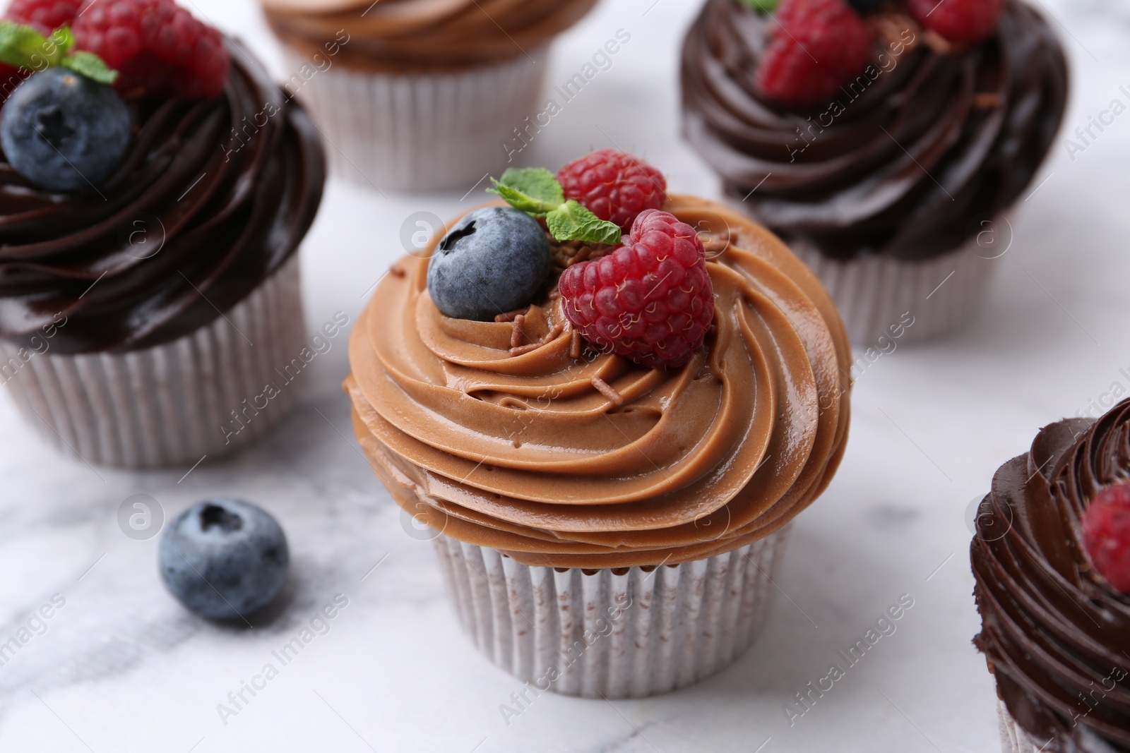 Photo of Tasty cupcakes with chocolate cream and berries on white marble table, closeup