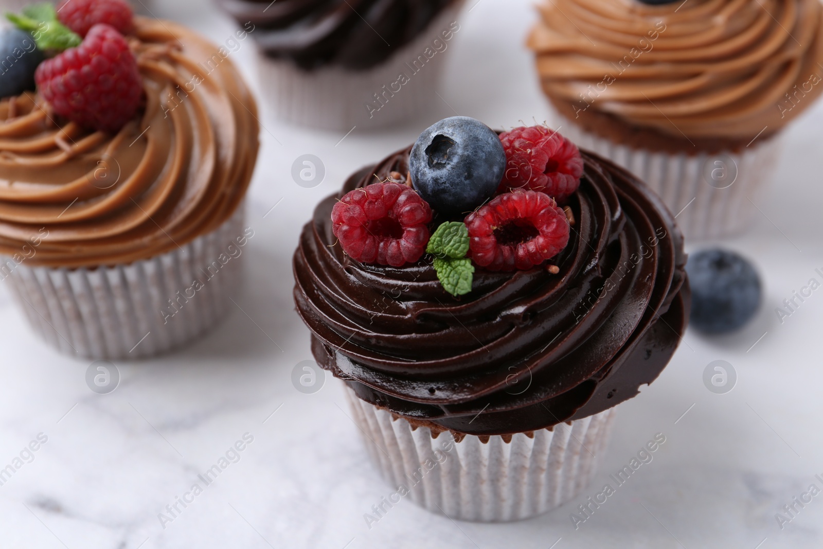 Photo of Tasty cupcakes with chocolate cream and berries on white marble table, closeup