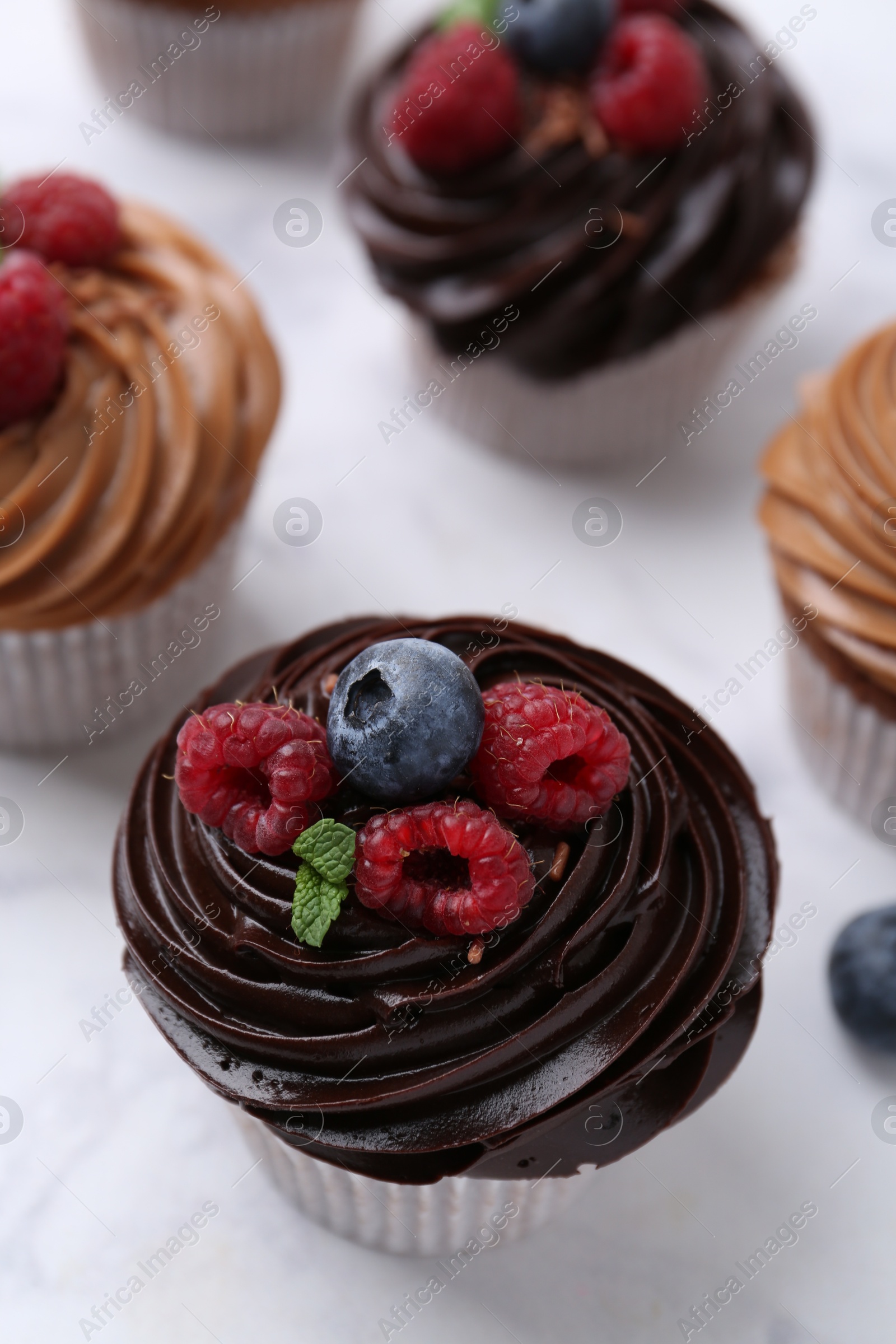 Photo of Tasty cupcakes with chocolate cream and berries on white marble table, closeup