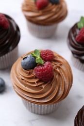 Photo of Tasty cupcakes with chocolate cream and berries on white marble table, closeup