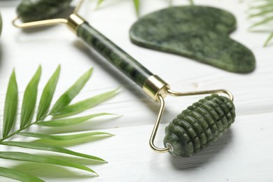 Photo of Face roller, gua sha tool and palm leaf on white wooden background, closeup